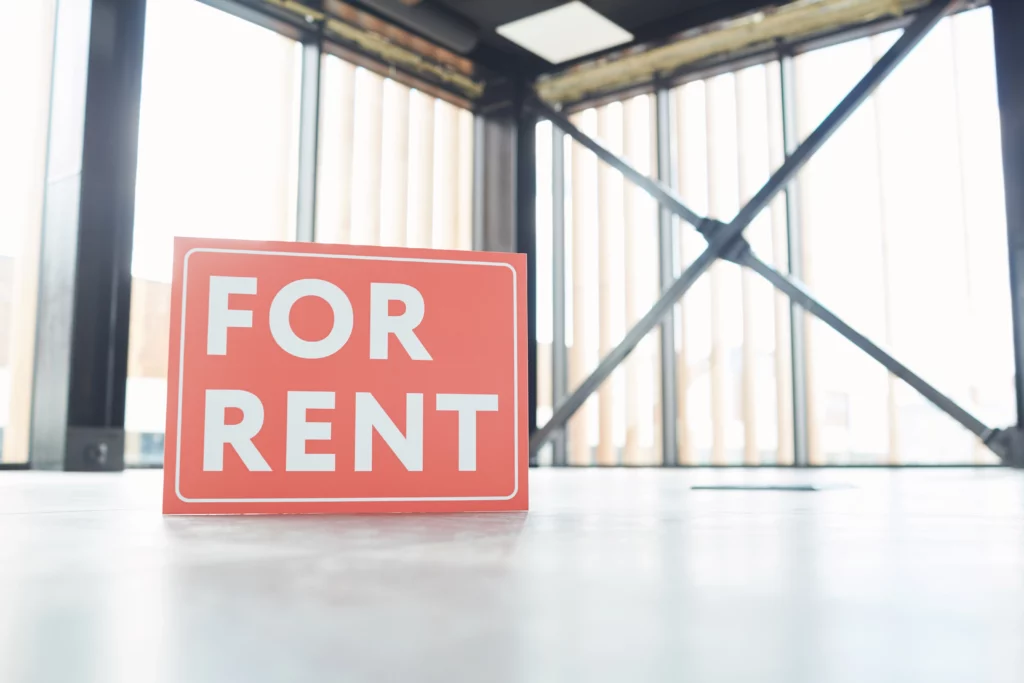 Red For Rent sign on shiny floor in an empty, industrial-style room with large windows and exposed metal beams