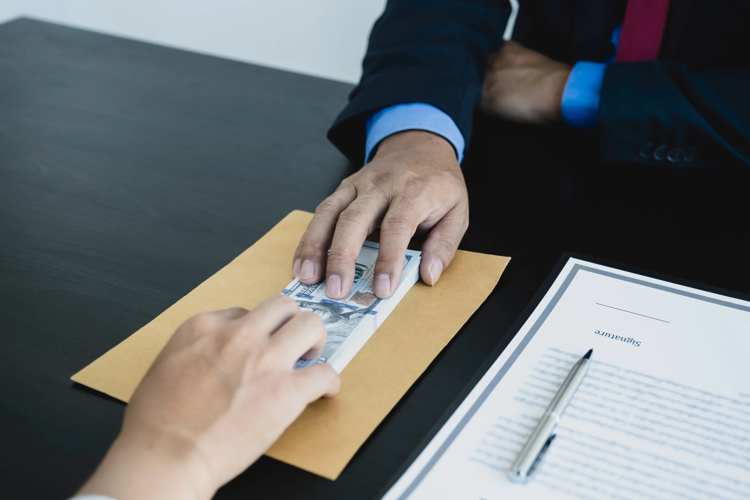 Two hands exchanging cash over a contract, symbolizing a security deposit return in a rental agreement.
